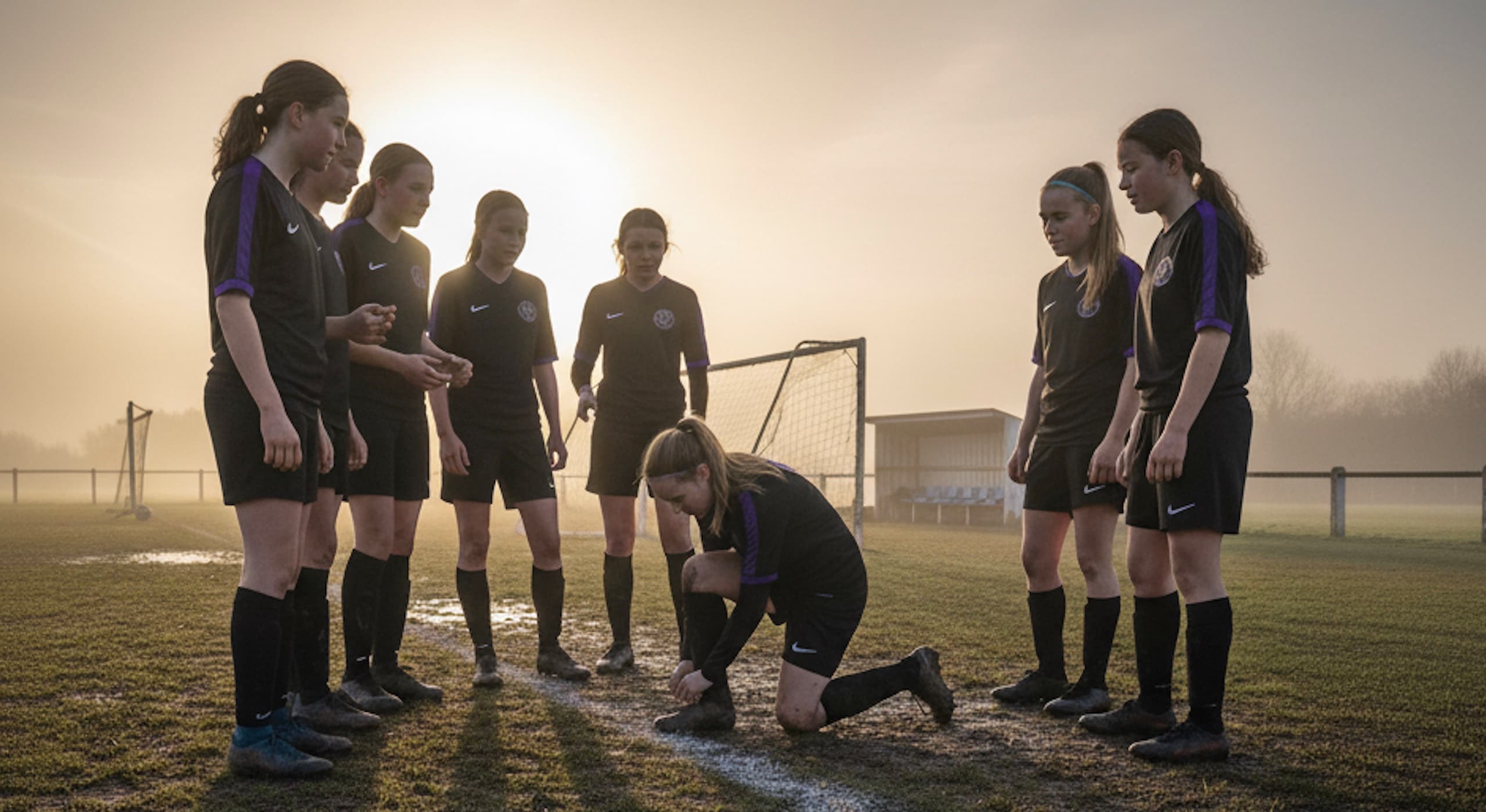 Girls football team in team huddle on pitch during golden hour training session, representing the unity and potential highlighted in the 2025 Sky report on closing the UK girls sport participation gap