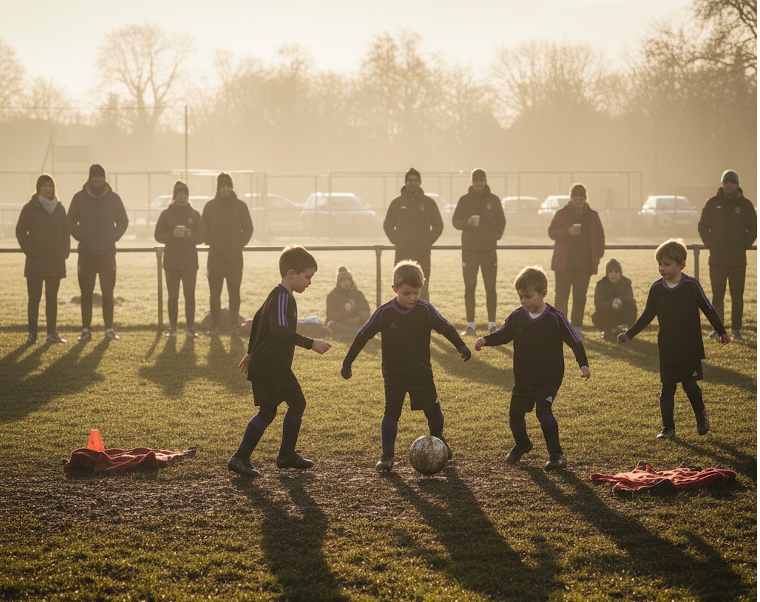 Young football players training in golden light with parents and coaches watching from the sidelines, representing the grassroots football community that Future Fit reforms aim to support and develop